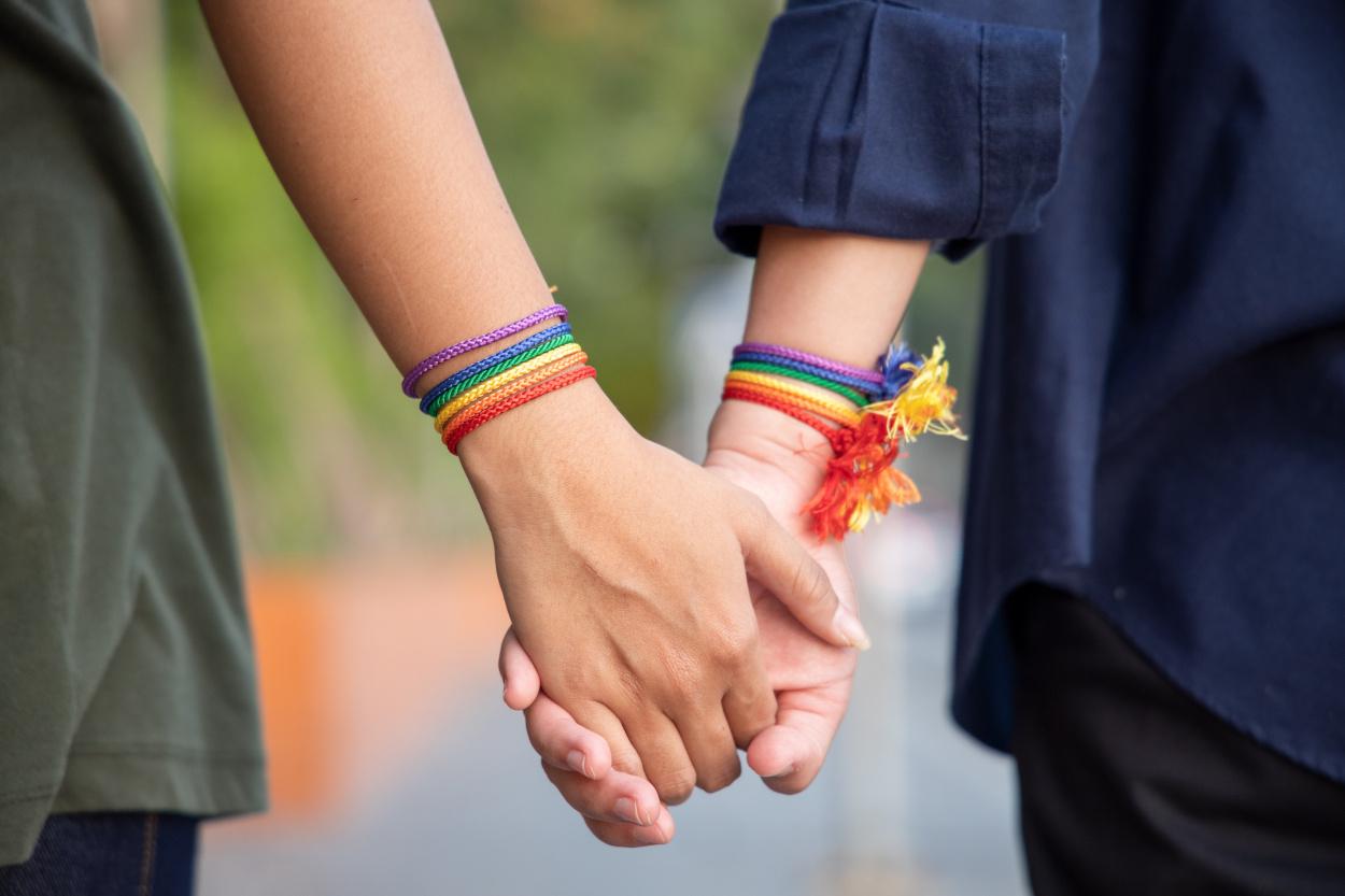 Deux mains féminines qui se tiennent par la main avec des bracelets aux couleurs LGBT